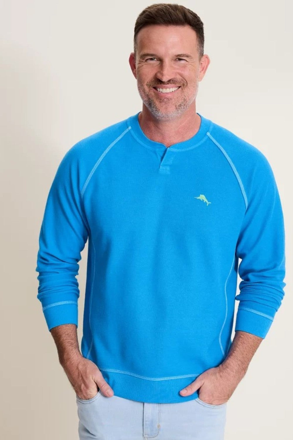 Man wearing a blue long-sleeve shirt with a logo on a beige background