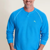 Man wearing a blue long-sleeve shirt with a logo on a beige background