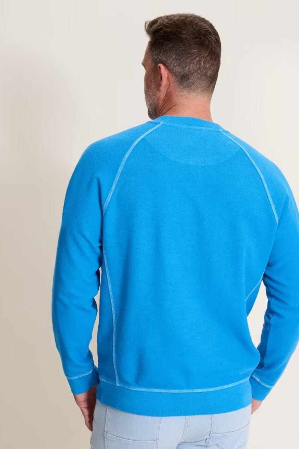 Man wearing a blue sweatshirt with white piping on a plain background