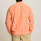 Person wearing an orange sweater and beige shorts on a plain background