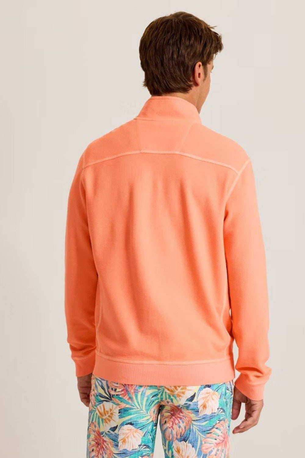 Person wearing an orange half-zip sweatshirt with floral pants on a plain background