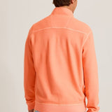 Person wearing an orange half-zip sweatshirt with floral pants on a plain background
