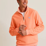 Man wearing an orange pullover with a logo on a plain background