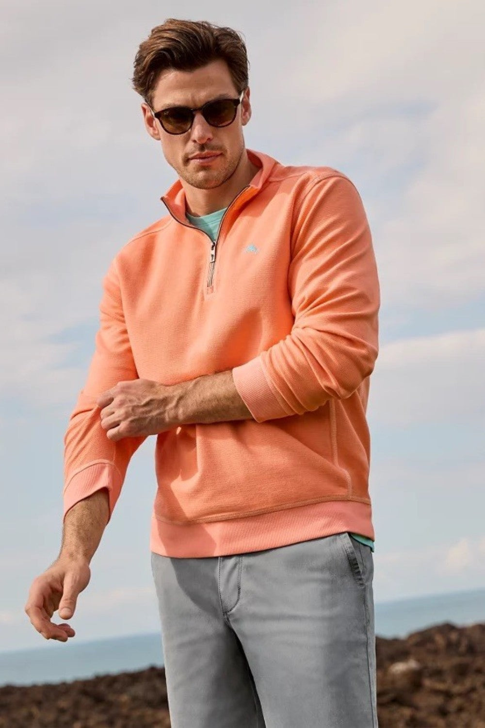 Man wearing an orange pullover with sunglasses and a neutral background