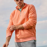 Man wearing an orange pullover with sunglasses and a neutral background