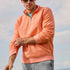Man wearing an orange pullover with sunglasses and a neutral background
