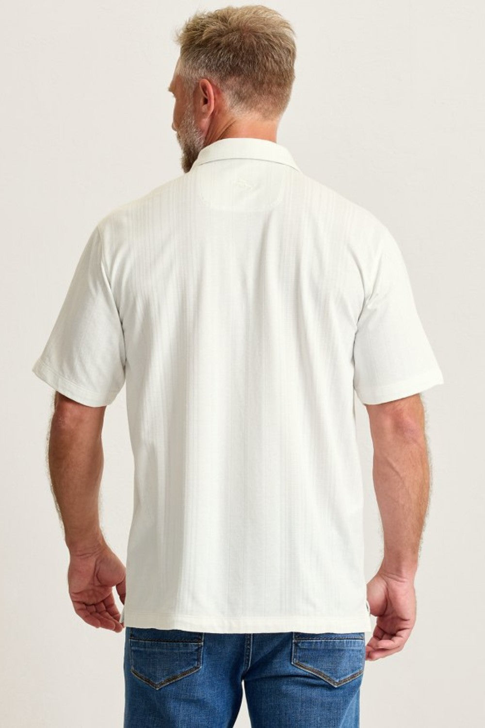 Man wearing a white polo shirt and blue jeans on a plain background