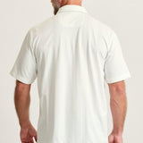 Man wearing a white polo shirt and blue jeans on a plain background