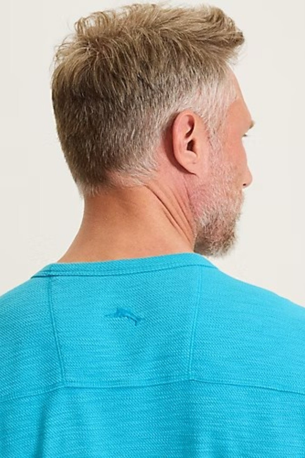 Man wearing a blue polo shirt with a small logo on a plain background