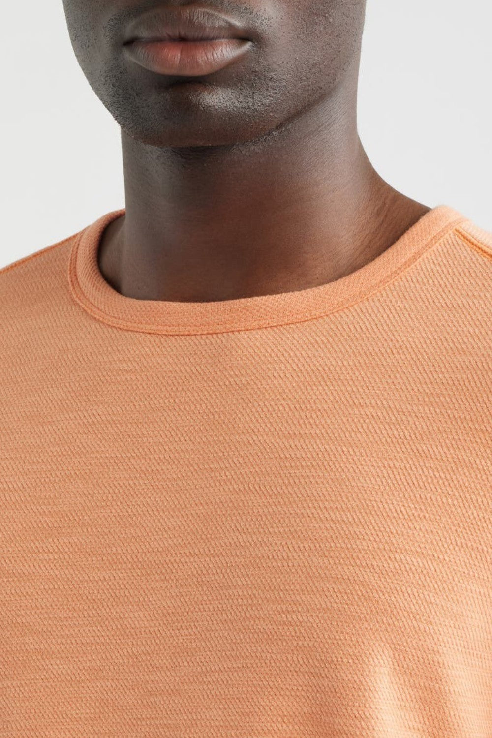 Close-up of a person wearing an orange sweater against a light background
