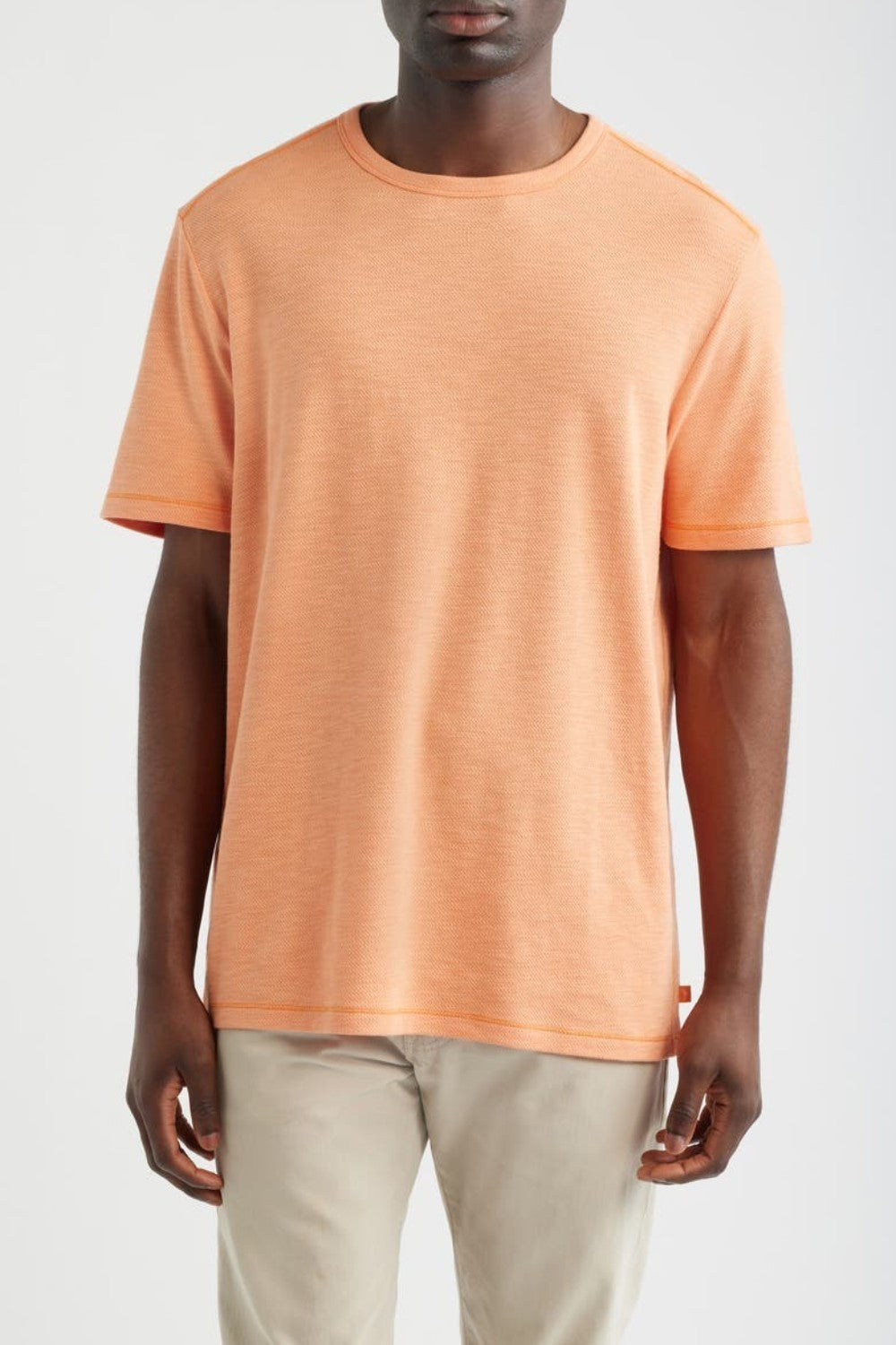 Person wearing an orange t-shirt and beige pants on a white background
