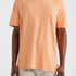 Person wearing an orange t-shirt and beige pants on a white background
