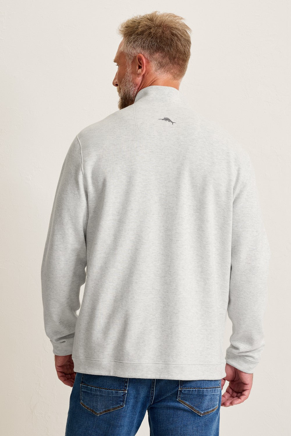 Man wearing a light gray long-sleeve shirt with a small logo on the back against a plain background