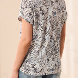 Person wearing a patterned top and jeans against a beige background
