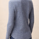 Person wearing a blue textured top and jeans against a beige background