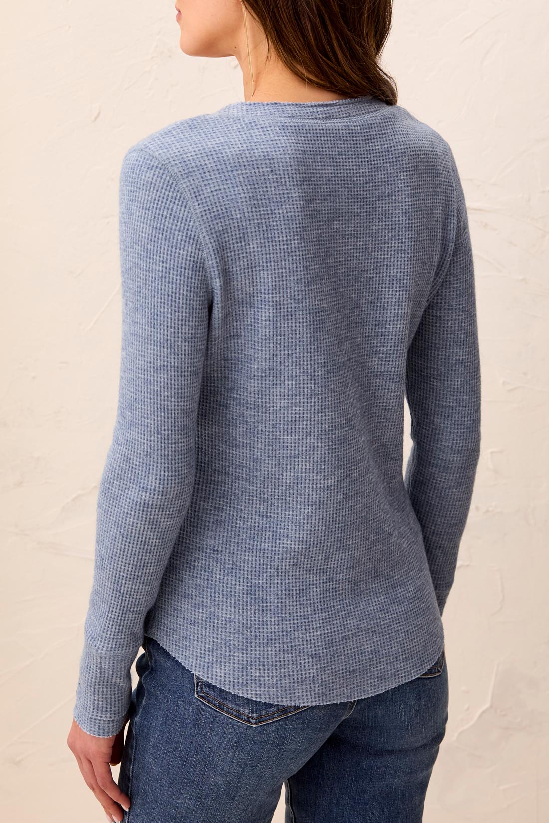 Person wearing a blue textured top and jeans against a beige background