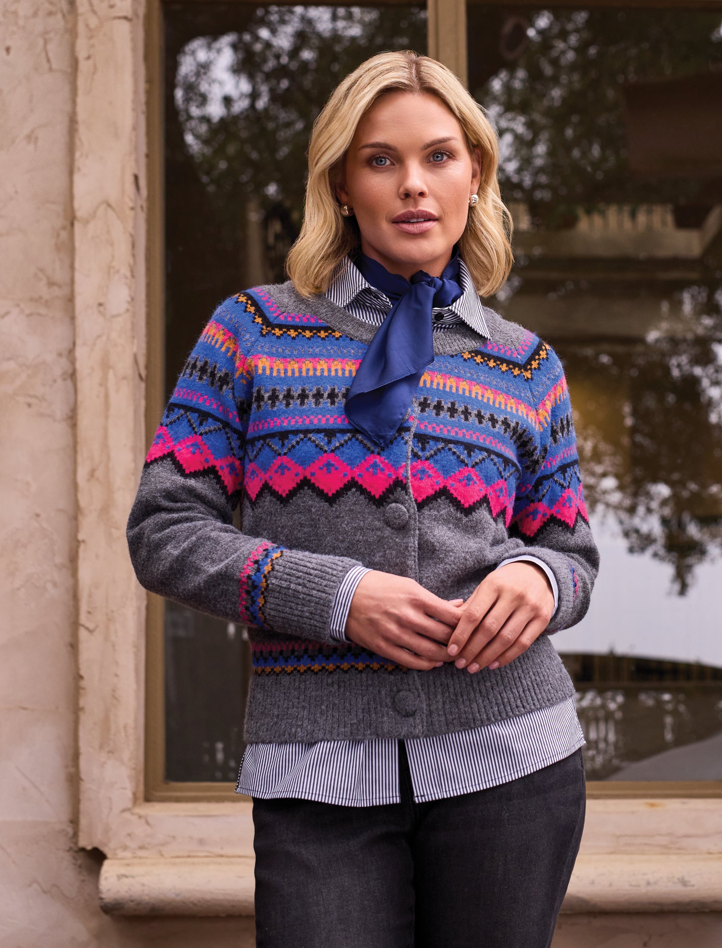 Woman wearing a patterned sweater over a striped shirt standing outdoors.