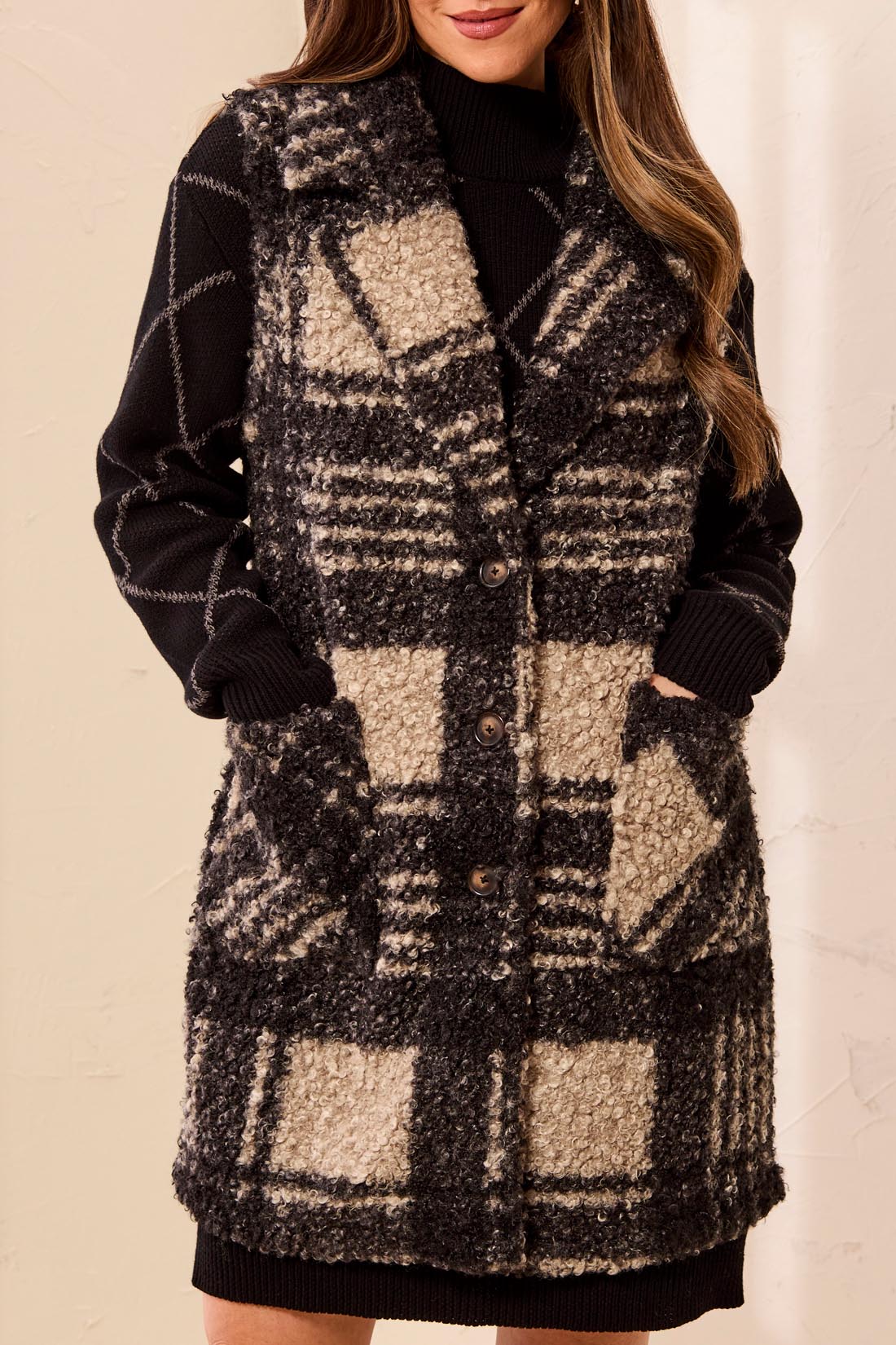 Woman wearing a black and tan plaid vest with a button front and functional pockets over a black dress against a light backdrop.