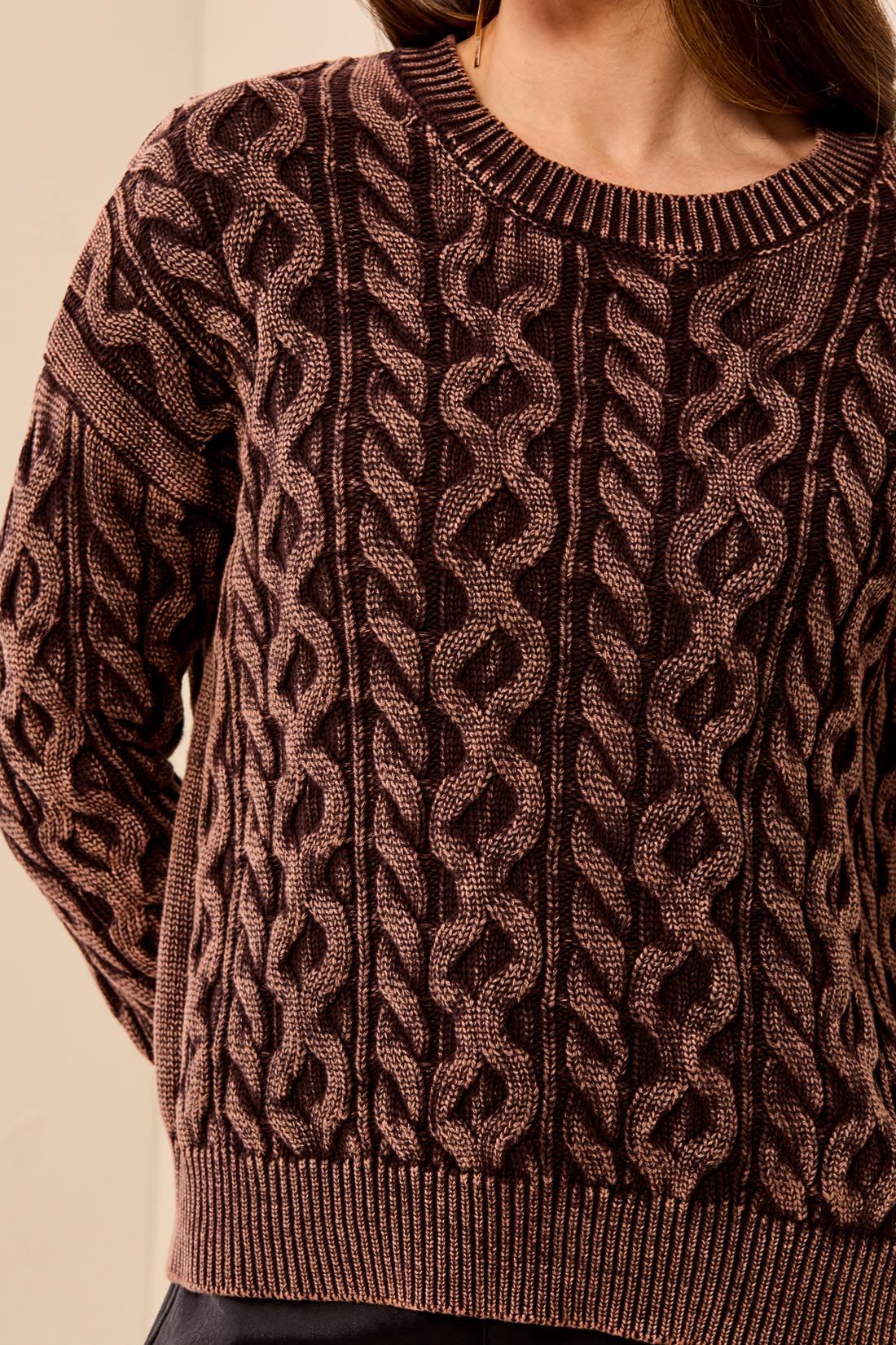 Close-up of a brown cable knit sweater on a neutral background