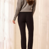 Woman wearing a gray sweater and black pants against a white curtain background