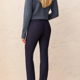 Person wearing a blue patterned top and navy pants against a light beige wall.