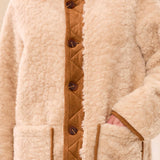 Person wearing a beige sherpa jacket with brown buttons on a plain background