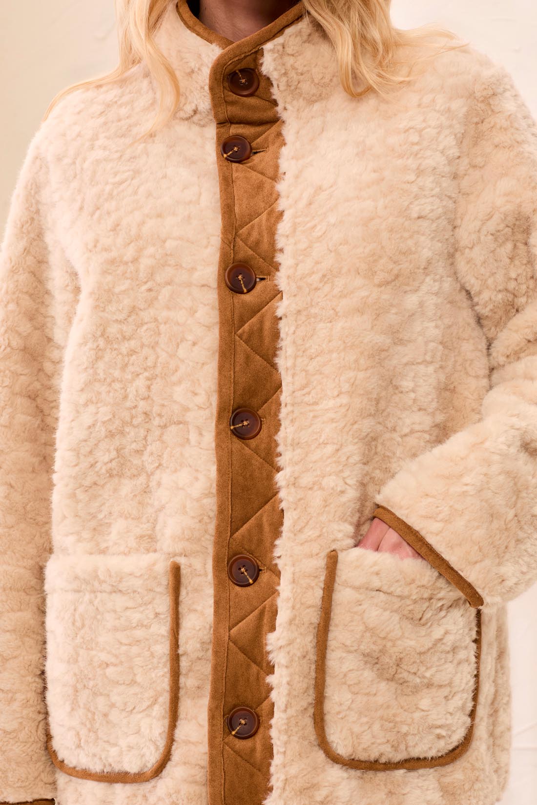 Person wearing a beige sherpa jacket with brown buttons on a plain background