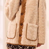 Person wearing a beige sherpa jacket with brown buttons on a plain background
