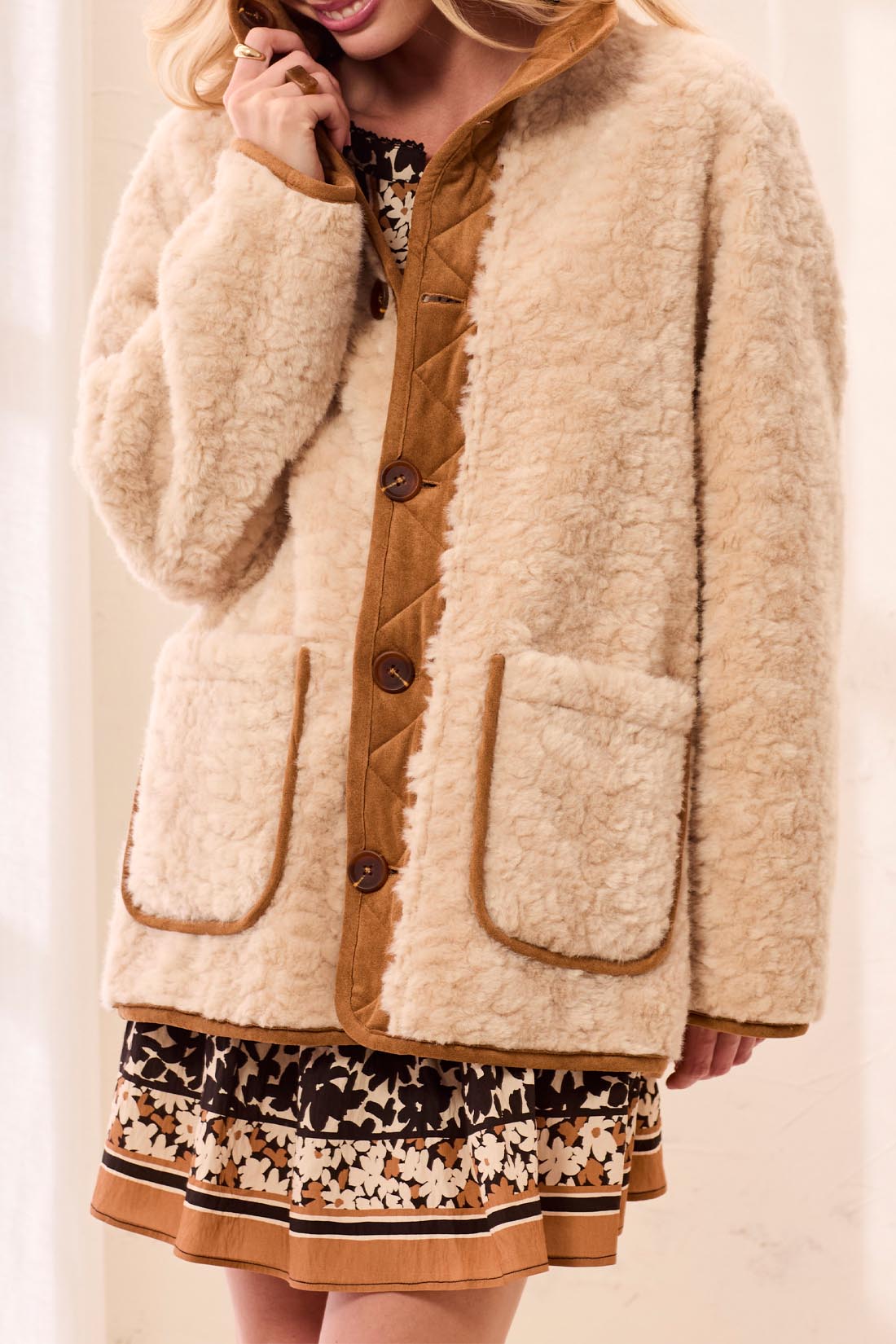 Person wearing a beige sherpa jacket with brown buttons on a plain background