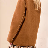 Person wearing a brown coat over a floral dress on a beige background