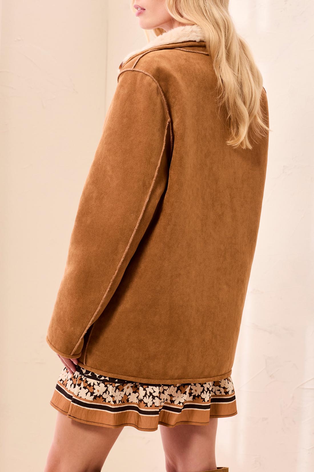 Person wearing a brown coat over a floral dress on a beige background