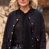 Black polka dot blouse worn under a black jacket with blue jeans, with a black belt, on person in an outdoor setting.