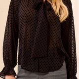 Black polka dot blouse worn by a person on a beige background