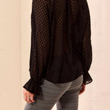 Black polka dot blouse worn by a person on a beige background