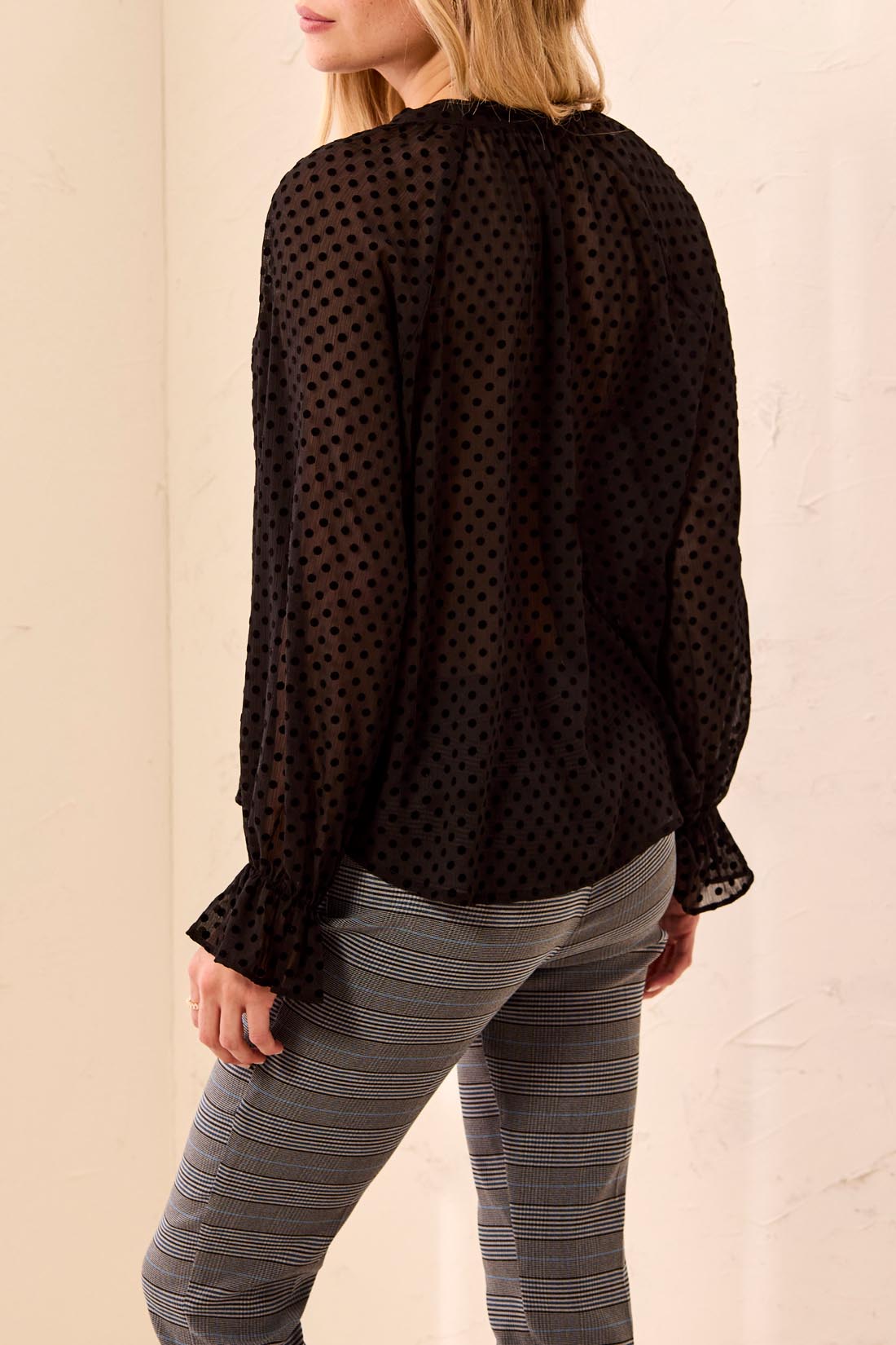 Black polka dot blouse worn by a person on a beige background