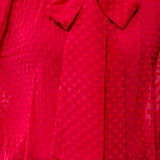A close-up of a bright pink sheer blouse with a subtle tonal polka dot pattern and a large bow at the neckline.