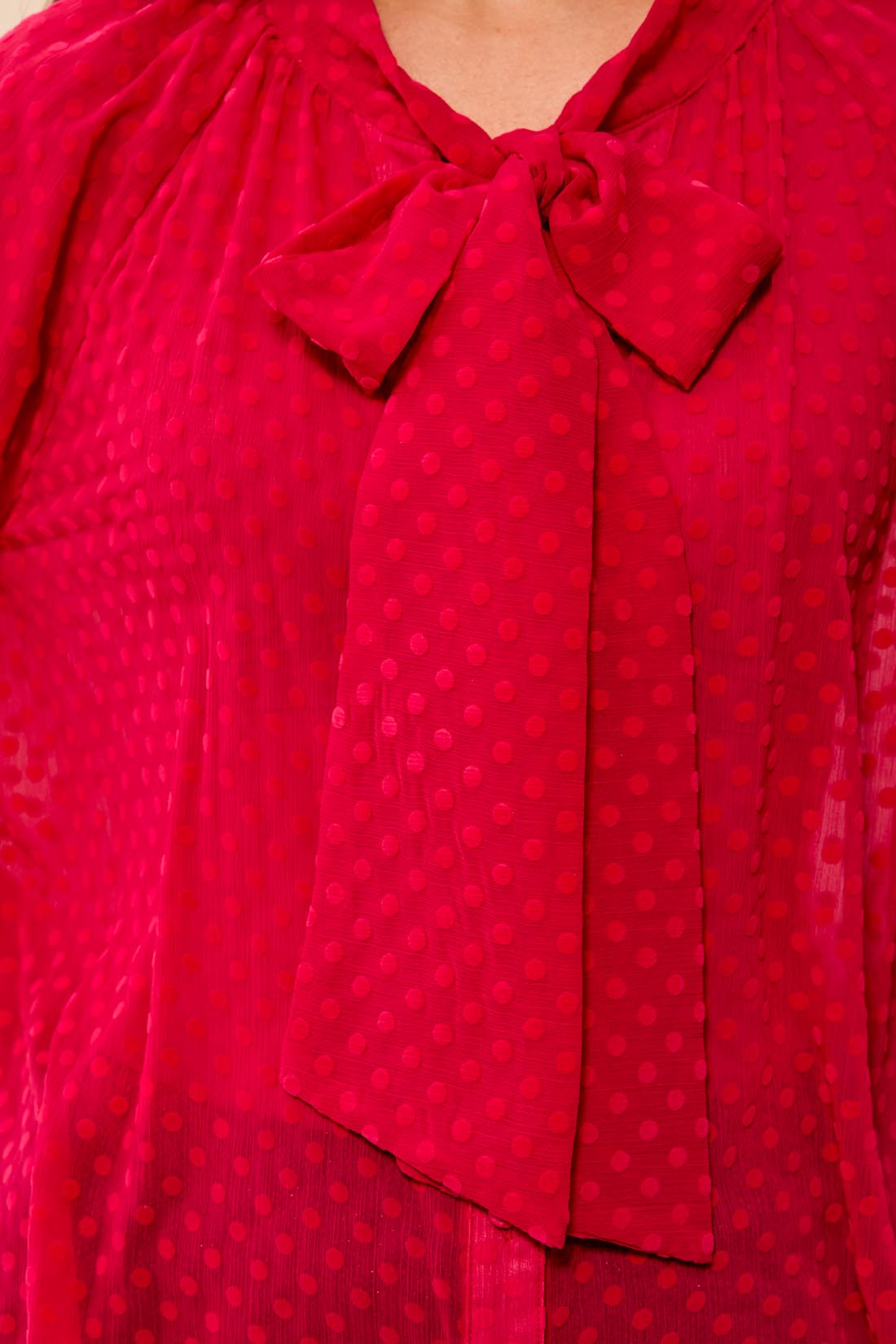 A close-up of a bright pink sheer blouse with a subtle tonal polka dot pattern and a large bow at the neckline.