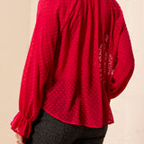 A woman wearing a bright pink long-sleeve blouse with a subtle polka dot pattern, shown from the back. The blouse features a gathered high neck and ruffled cuffs.