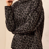 Woman wearing a black and grey animal print top with black pants against a light backdrop.