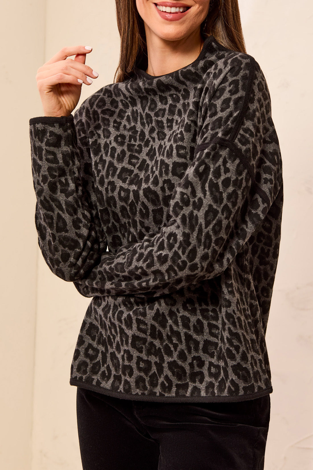 Woman wearing a black and grey animal print top with black pants against a light backdrop.