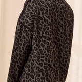 Woman, shown from the back, wearing a black and grey animal print top with black pants against a light backdrop.