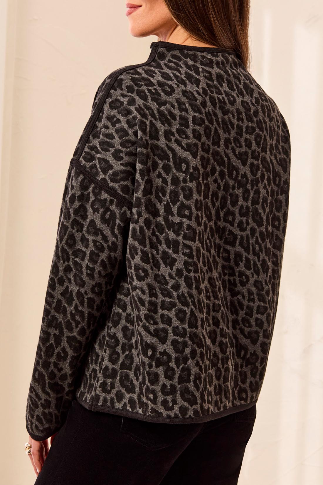 Woman, shown from the back, wearing a black and grey animal print top with black pants against a light backdrop.