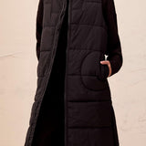Black quilted vest worn by a person on a beige background