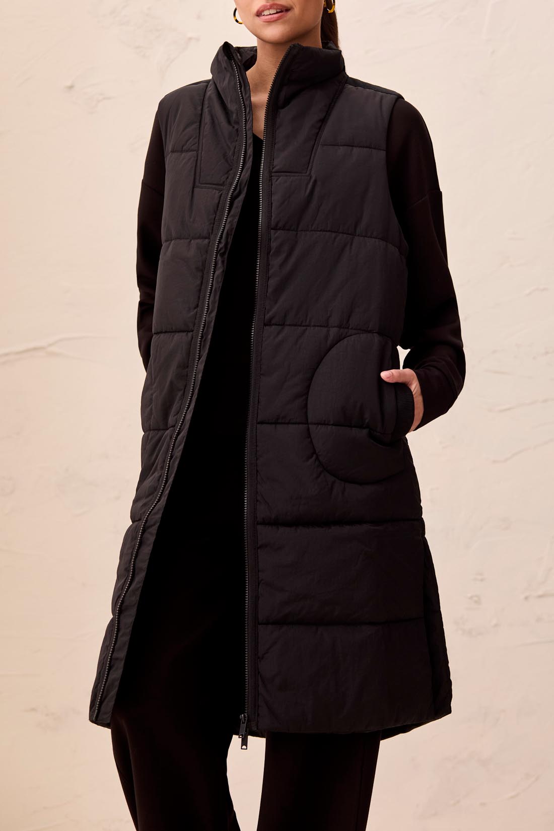 Black quilted vest worn by a person on a beige background