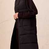 Person wearing a long black puffer vest against a plain background