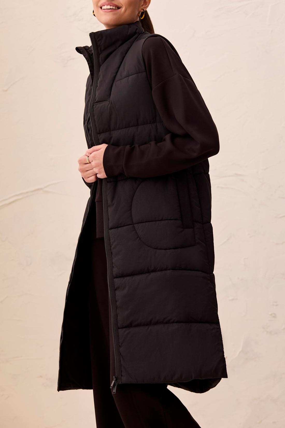 Person wearing a long black puffer vest against a plain background