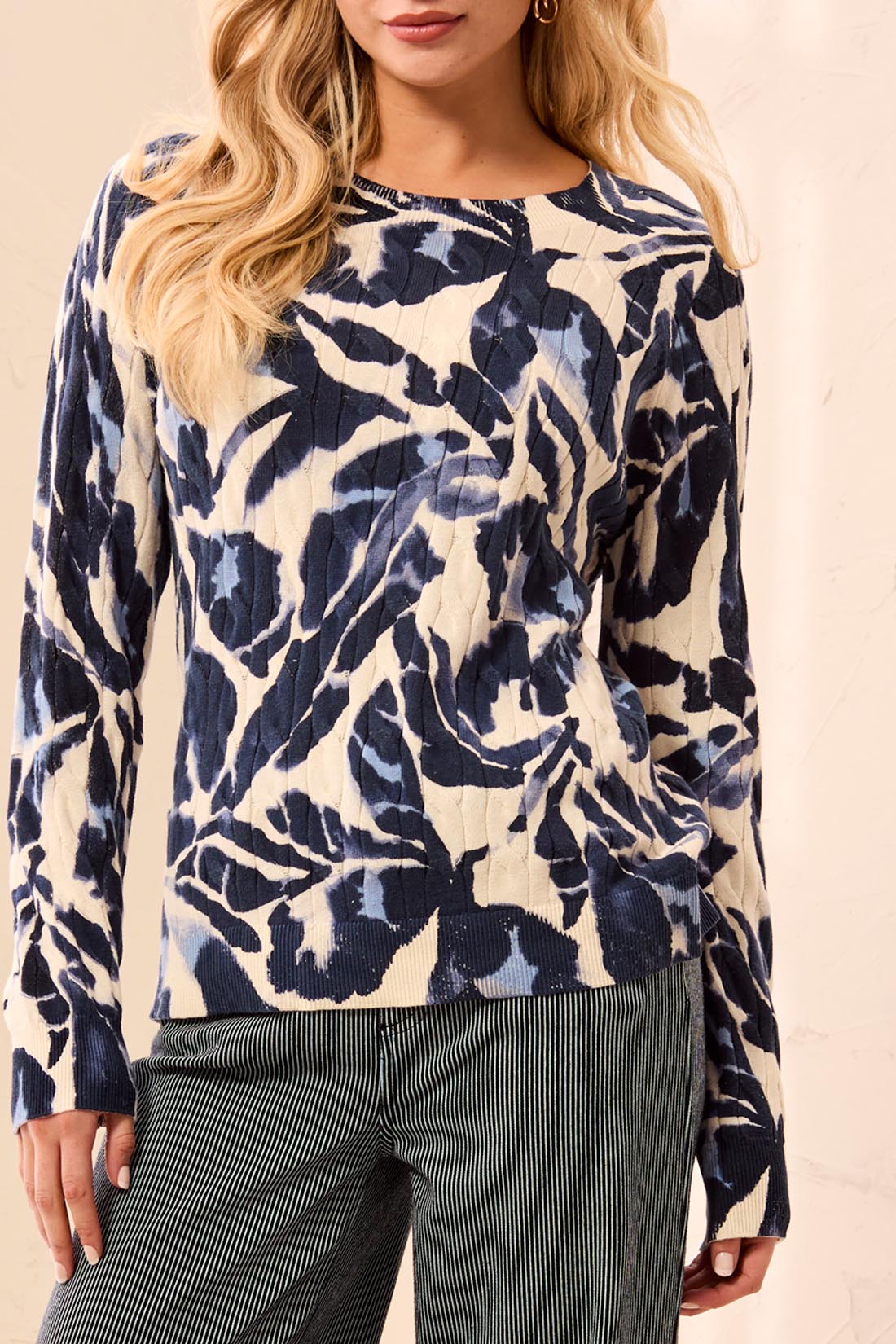 Woman wearing a blue and beige patterned sweater with striped pants on a light background