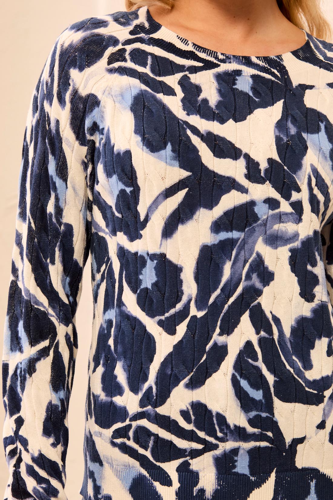 Woman wearing a blue and beige patterned sweater with striped pants on a light background