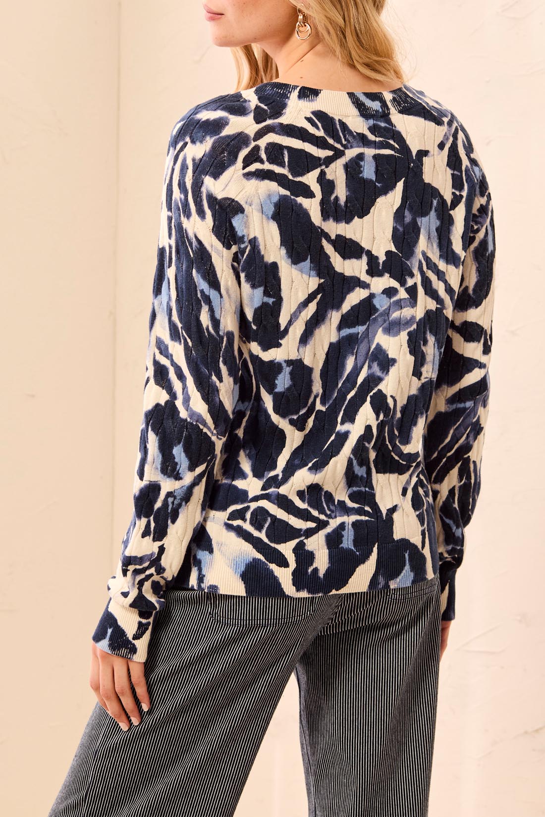 Woman wearing a blue and beige patterned sweater with striped pants on a light background
