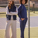 Two women standing on a tennis court wearing casual outfits.
